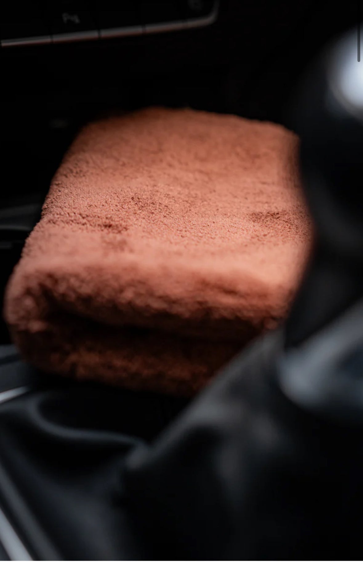 A folded FibreKing Ultimate Detailer Cloth in brown, from the 3 pack set, rests on a dark surface—possibly inside a vehicle—with part of a gear shift visible in the foreground.