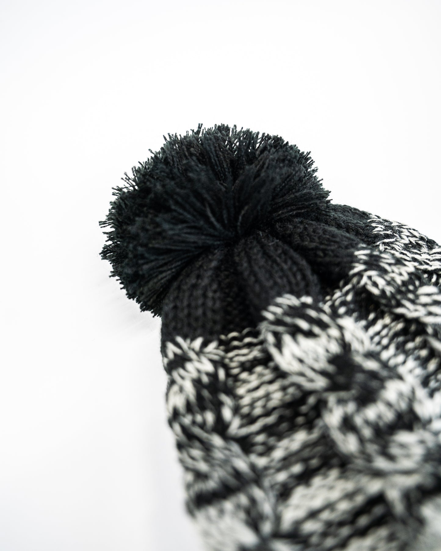 A close-up of the FibreKing Knitted Bobble Hat by FibreKing, in black and white with a large black pom-pom and heavyweight multi-yarn knit, shown against a white background.