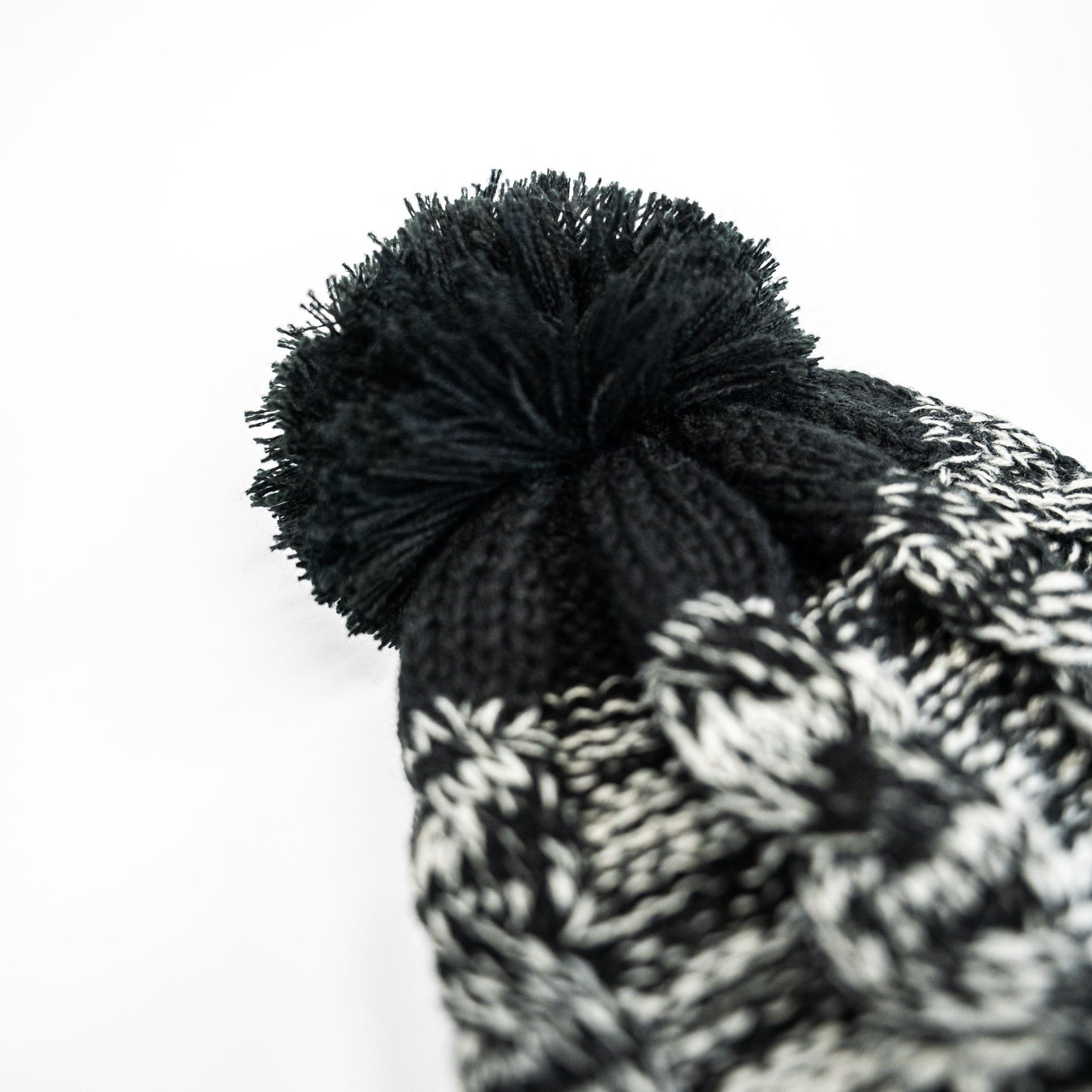 A close-up of the FibreKing Knitted Bobble Hat by FibreKing, in black and white with a large black pom-pom and heavyweight multi-yarn knit, shown against a white background.
