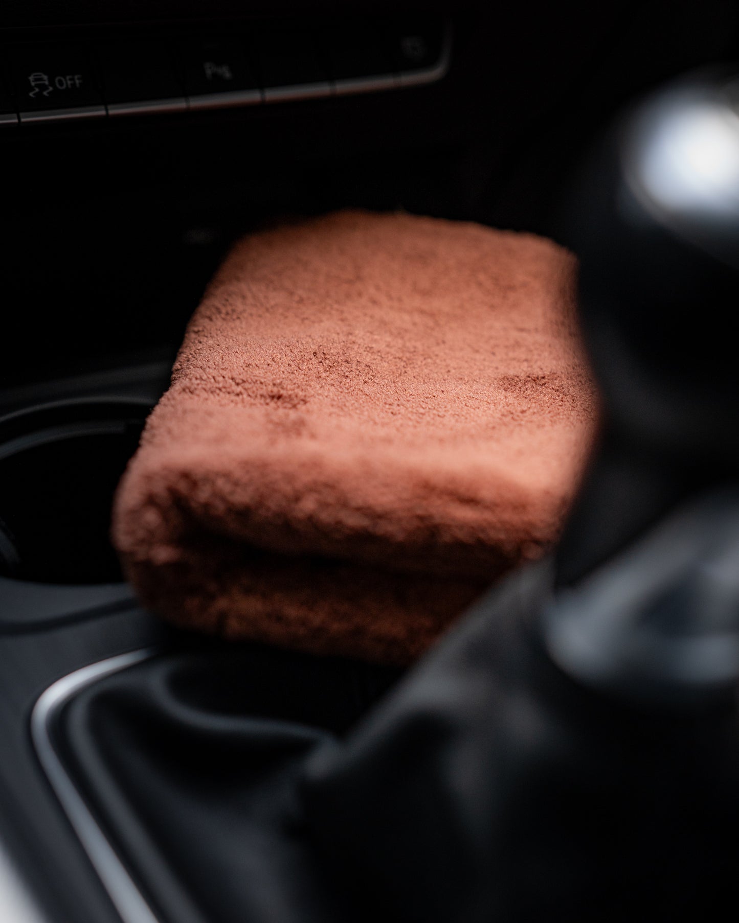 A folded brown Ultimate detailer cloth by FibreKing rests on the car’s center console beside the gear shift, ready to deliver a lint-free finish.