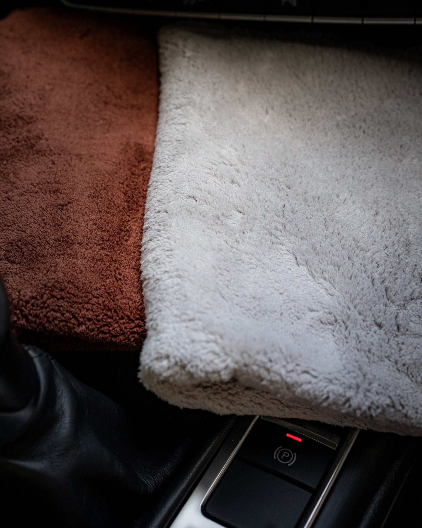 Close-up of a car interior featuring FibreKing's Ultimate detailer cloth in brown and white coral fleece microfiber, draped over the center console beside the electronic parking brake button.