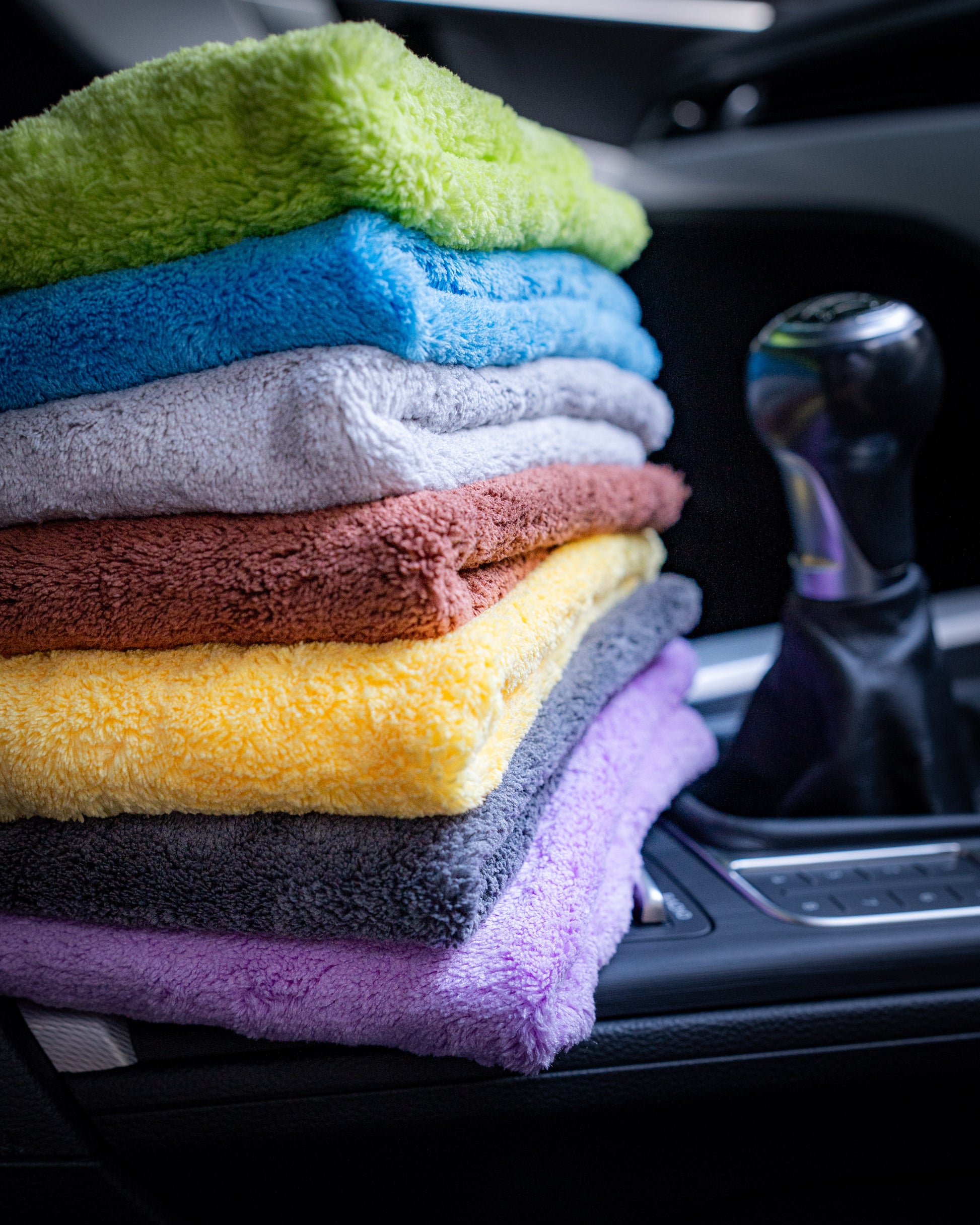 A stack of vibrant FibreKing Ultimate Detailer Cloths sits on a car’s center console beside the gear shift, ready to provide a flawless, lint-free finish.