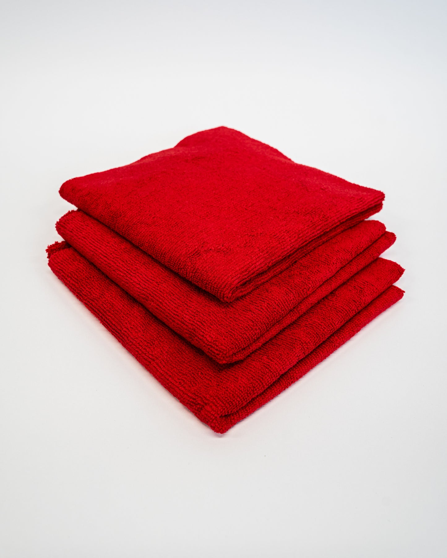 Three neatly folded red FibreKing Duplex Edgeless Cloths (3 pack) stacked on a white surface, perfect as dual pile microfibre detailing cloths for cleaning.