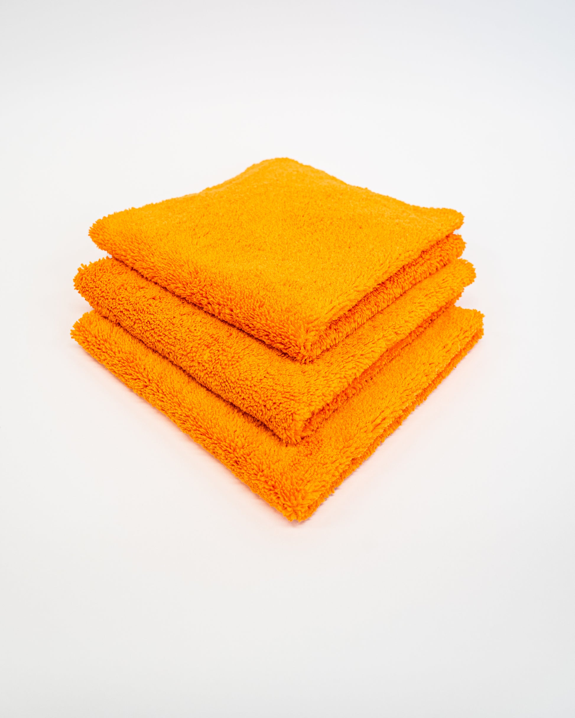 Three orange FibreKing Duplex edgeless cloths (3 pack) are neatly folded and stacked on a white surface.