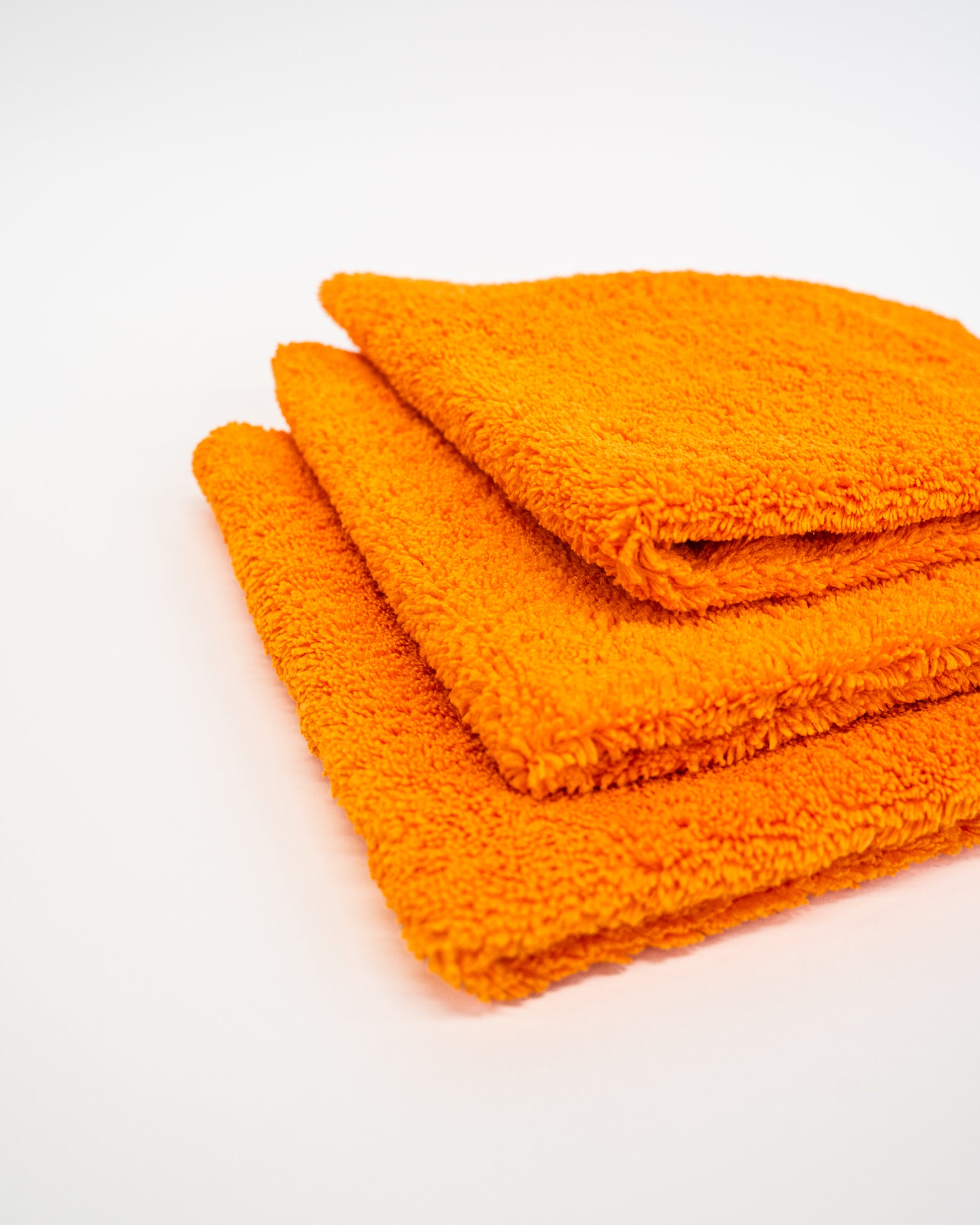 Three orange FibreKing Duplex edgeless cloths (3 pack), ideal as dual pile microfiber detailing cloths, are neatly stacked on a white surface.