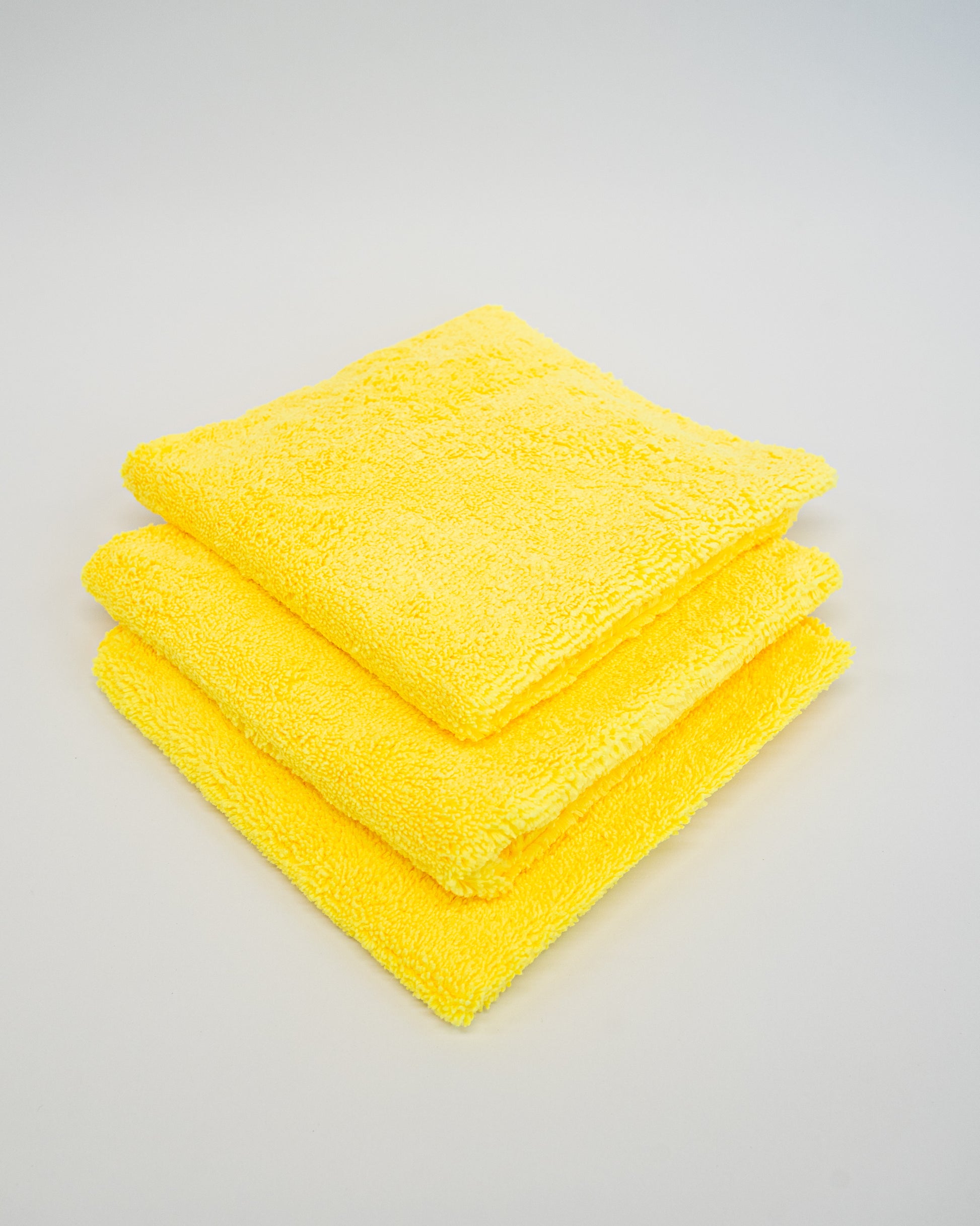 Three neatly folded yellow Duplex edgeless cloths by FibreKing, stacked on a white surface. This 3-pack of microfiber towels is perfect for spotless cleaning and detailing.