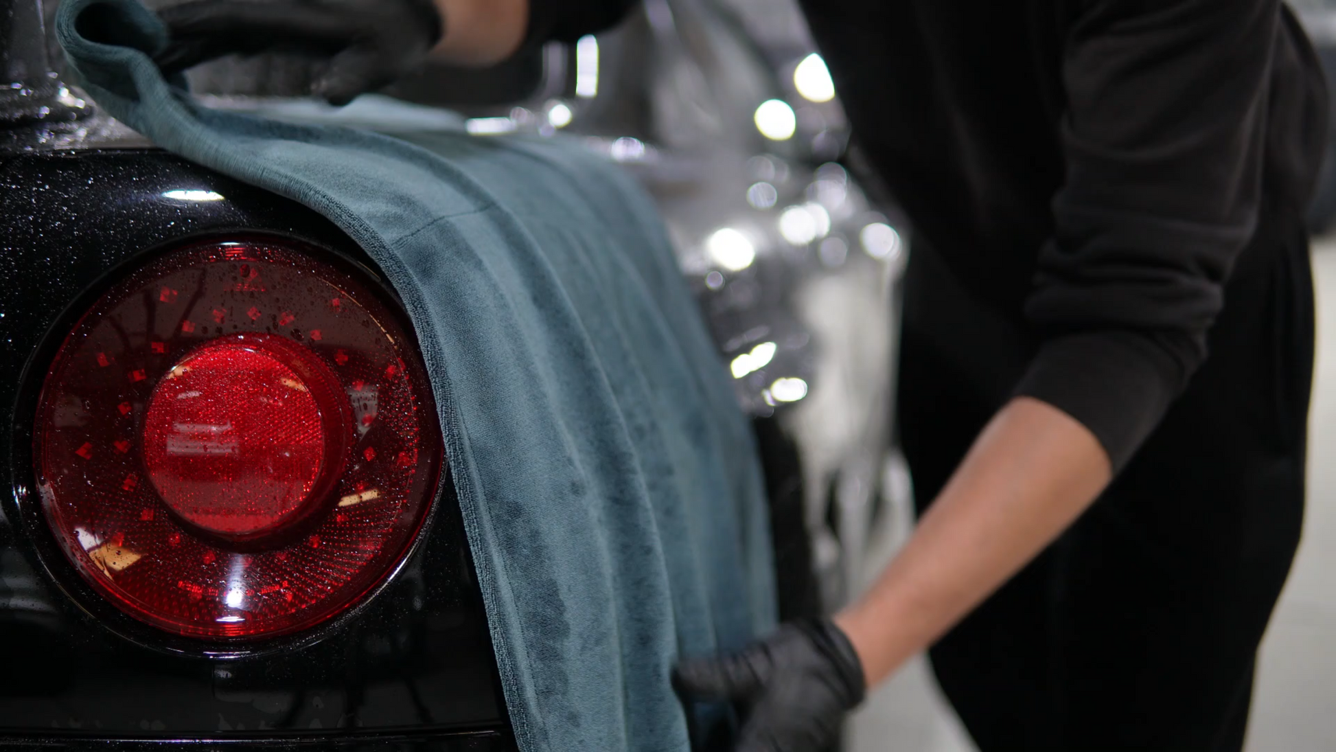 A person in black gloves wipes a black cars rear with the FibreKing Gold Label 900 GSM Korean Drying Towel, featuring an advanced microfiber blend for premium car care.