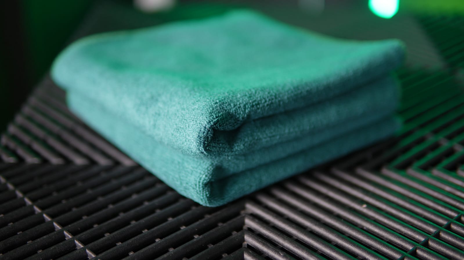 A folded green FibreKing microfiber towel from the Build Your Own Silver Label Pack rests on a black textured surface, ideal for customizing your microfibre cloth collection.