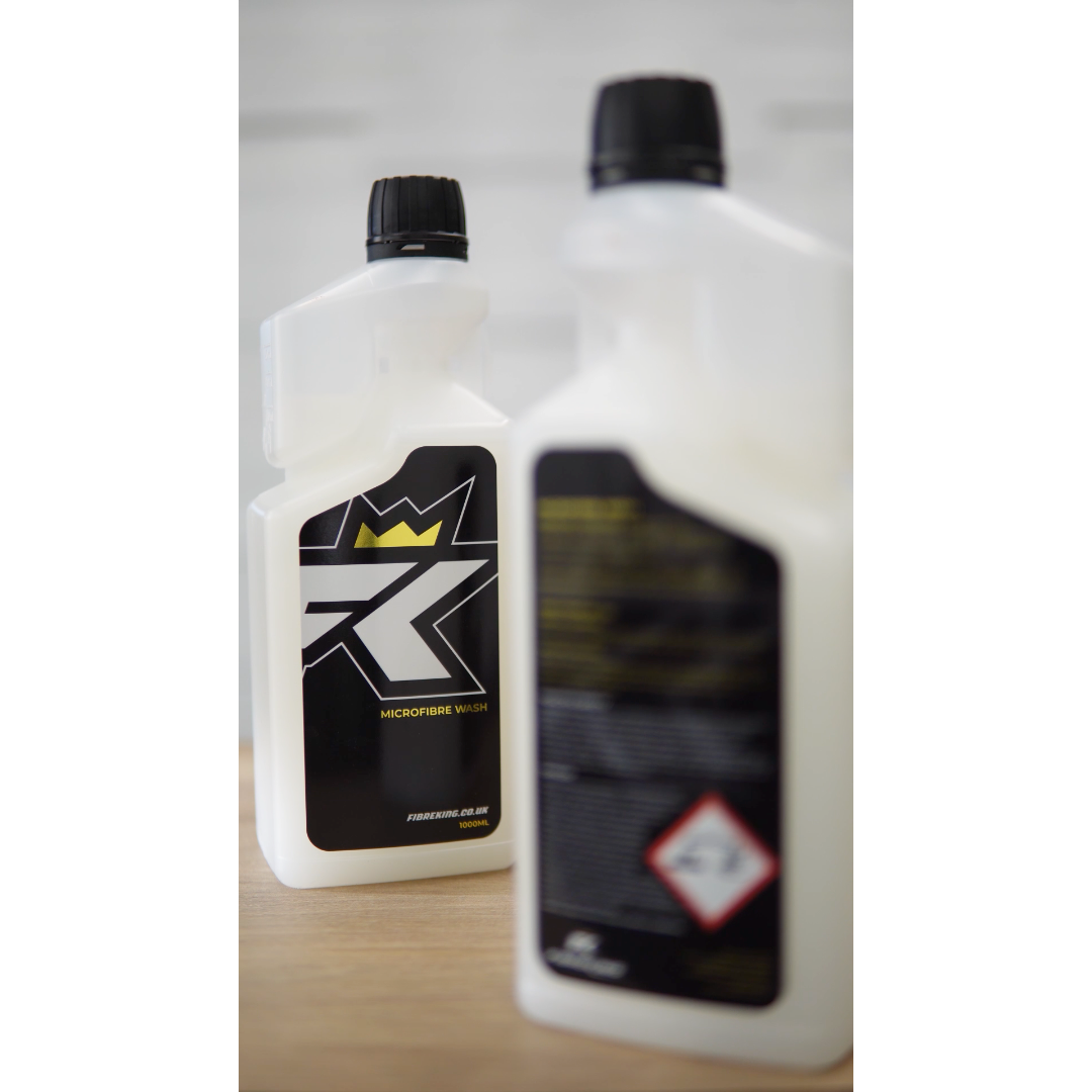 Two white FibreKing Microfibre Wash bottles with black caps—one focused showing the stylized R logo and crown, the other blurred with hazard symbols—ideal for caring for microfibre towels or as a detailing towel cleaner.