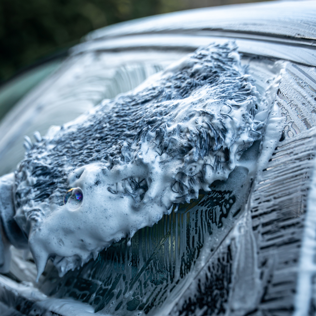 A close-up of the FibreKing Gold Label Korean Microfibre Wash Mitt - Grey cleaning a car window, with foam and water covering the glass for a swirl-free, premium wash.