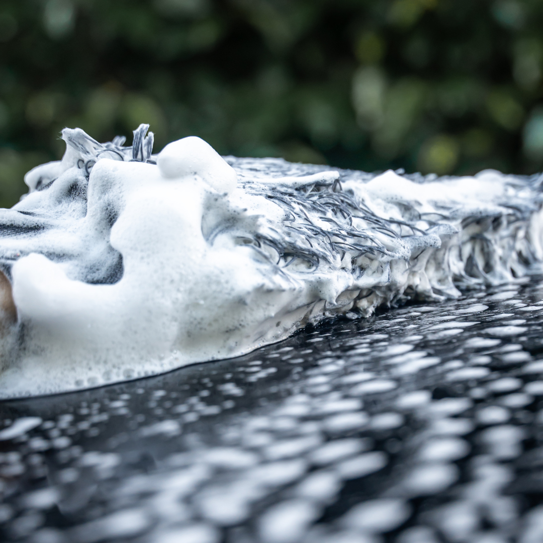 A close-up shows the FibreKing Gold Label Korean Microfibre Wash Mitt - Grey cleaning a black car with foam, using premium microfibres and dirt-trapping tech for a swirl-free finish.
