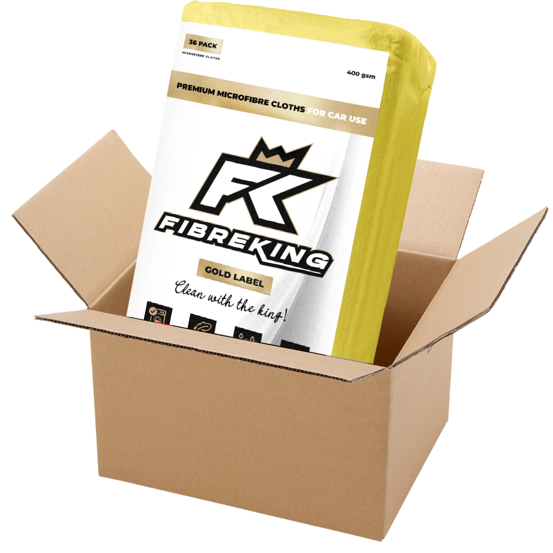 A FibreKing Gold Label 400GSM Microfibre Cloth Box (6 packs of 36) in yellow packaging is partially pulled out of an open brown cardboard shipping box.