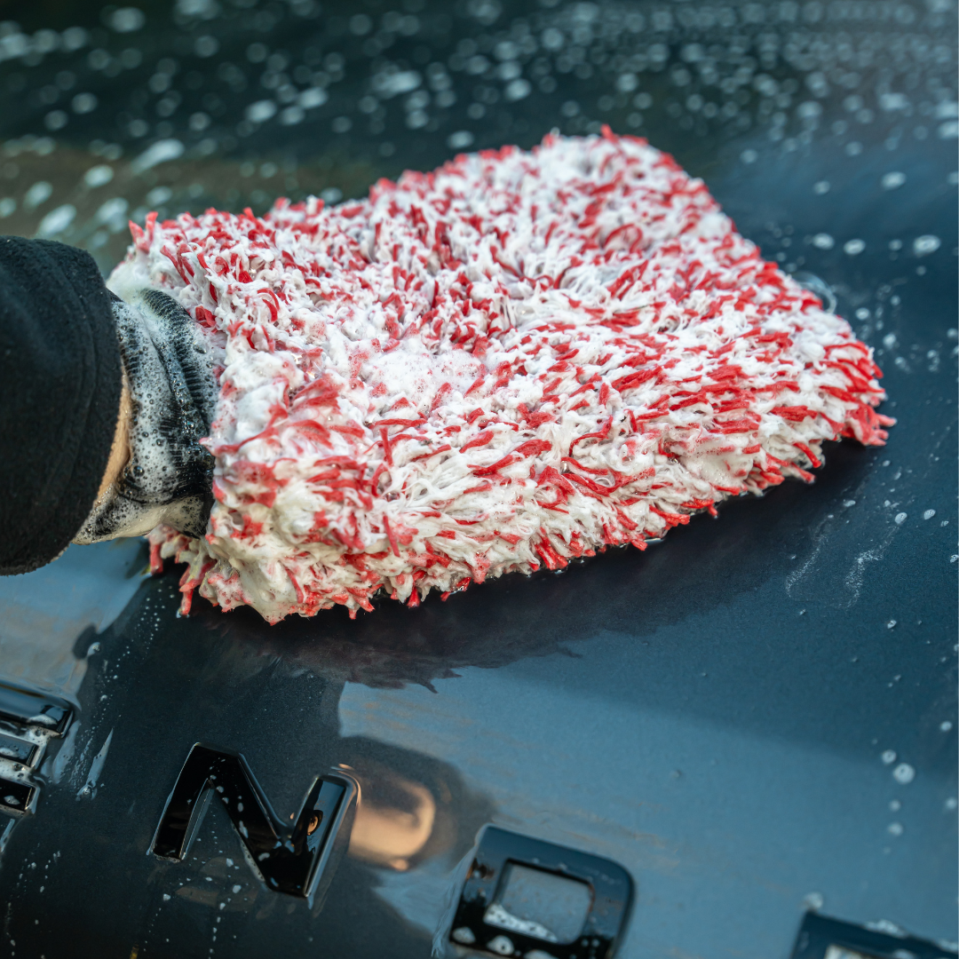 Washing a black car, a person uses the FibreKing SK Korean Microfibre Premium Wash Mitt in red, with advanced Dirt-Trapping Technology, creating soap suds on the vehicle’s surface.
