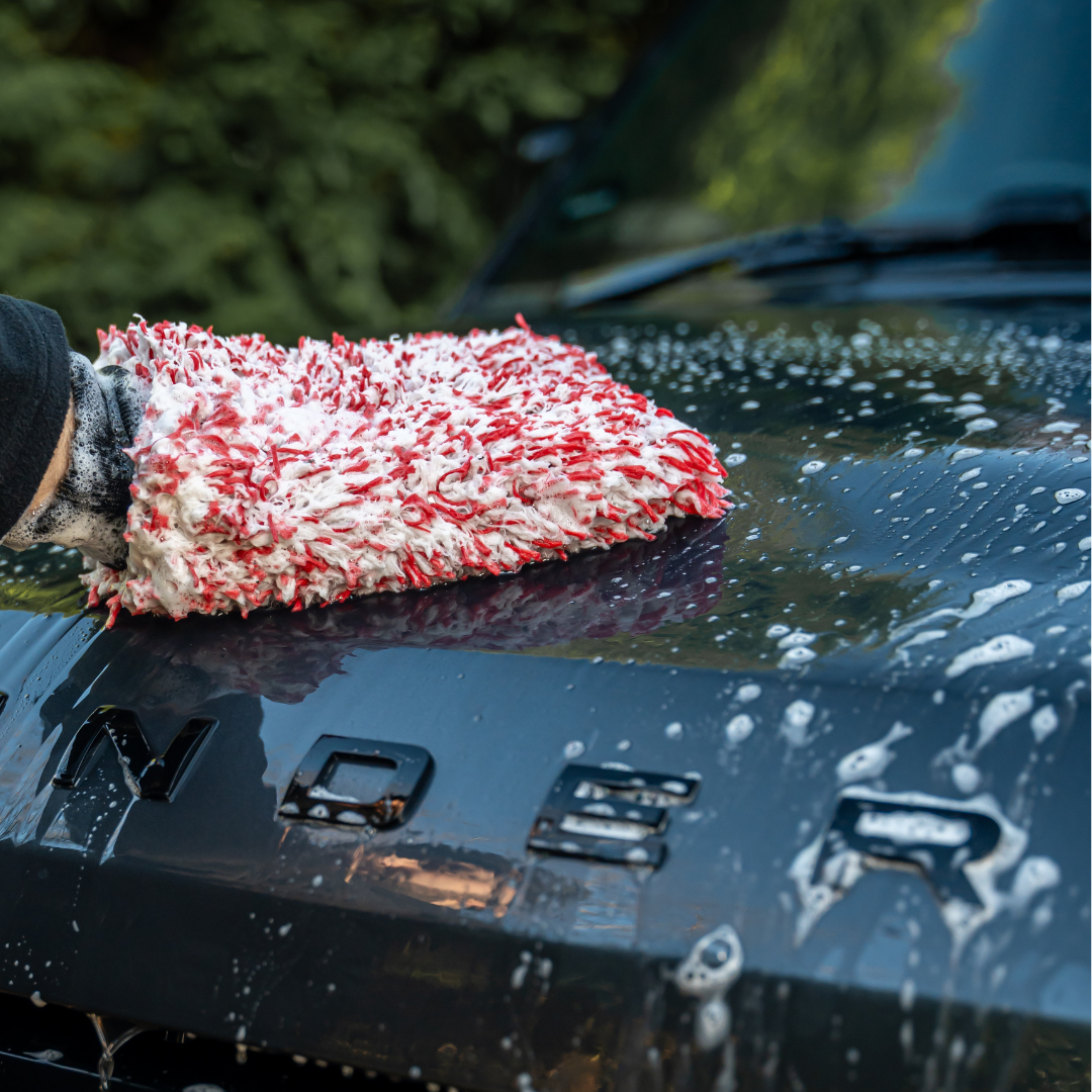 Someone uses the FibreKing SK Korean Microfibre Premium Wash Mitt - Red to gently wash the soapy black car hood outdoors.