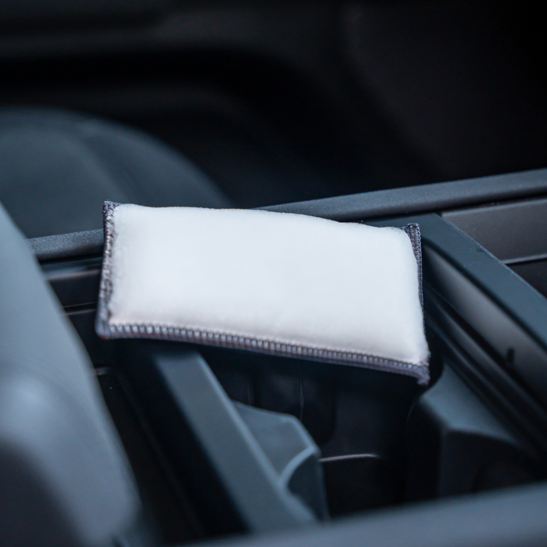 A small white rectangular FibreKing Scrub Pad from the 2 pack rests on a cars center console, its dark edges visible as part of a detailing kit.