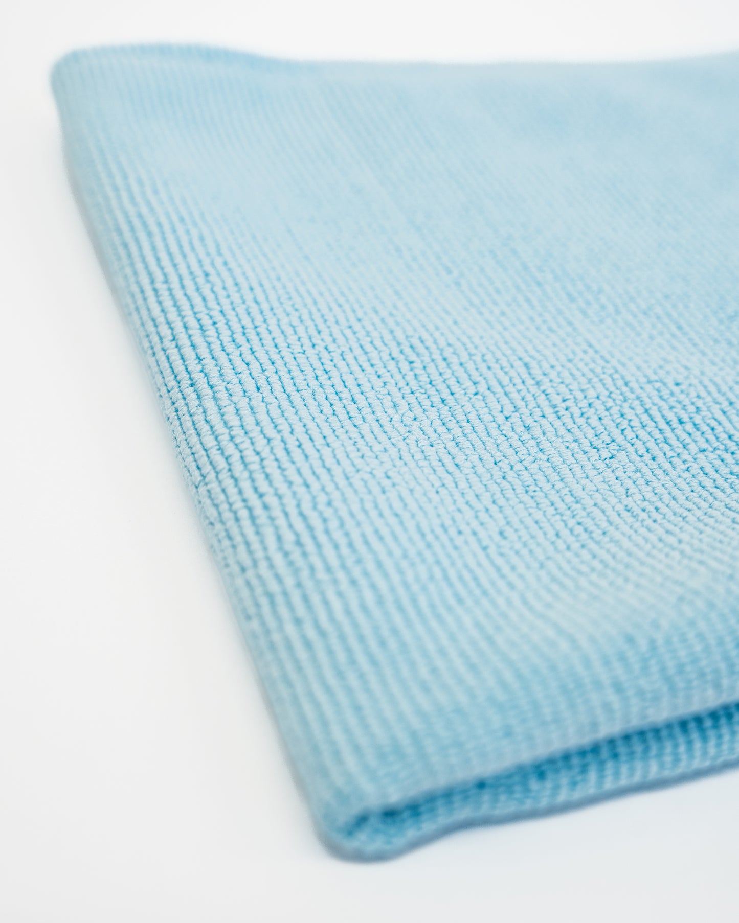 A close-up of the FibreKing Soft Edgeless Multi-Purpose Microfibre Cloth, folded in light blue on a white surface—perfect for detailing tasks.