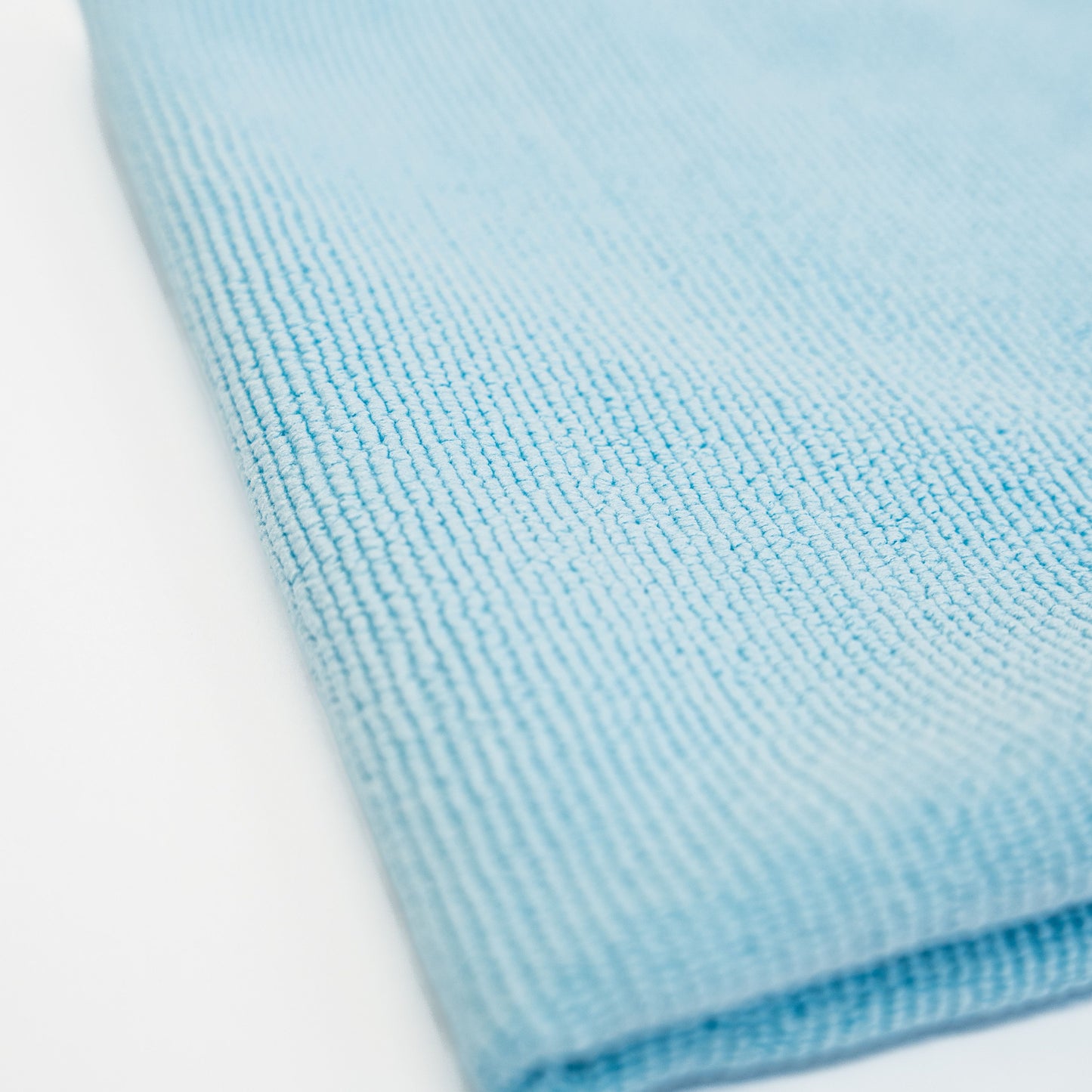 A close-up of the FibreKing Soft Edgeless Multi-Purpose Microfibre Cloth, folded in light blue on a white surface—perfect for detailing tasks.