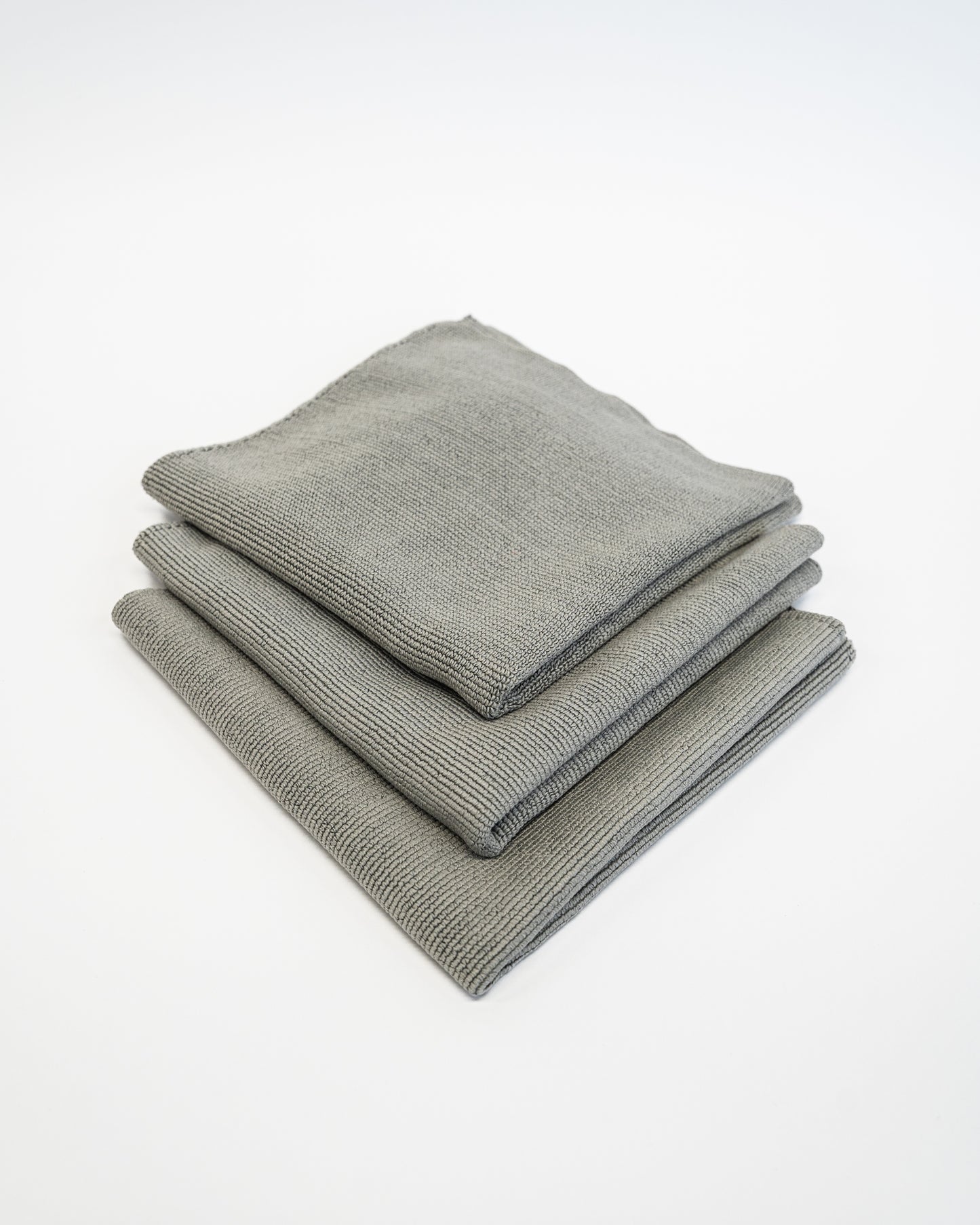 Three neatly stacked FibreKing Soft Edgeless Multi-Purpose Microfibre Cloths in gray lie on a white surface, ideal for streak-free detailing on any surface.
