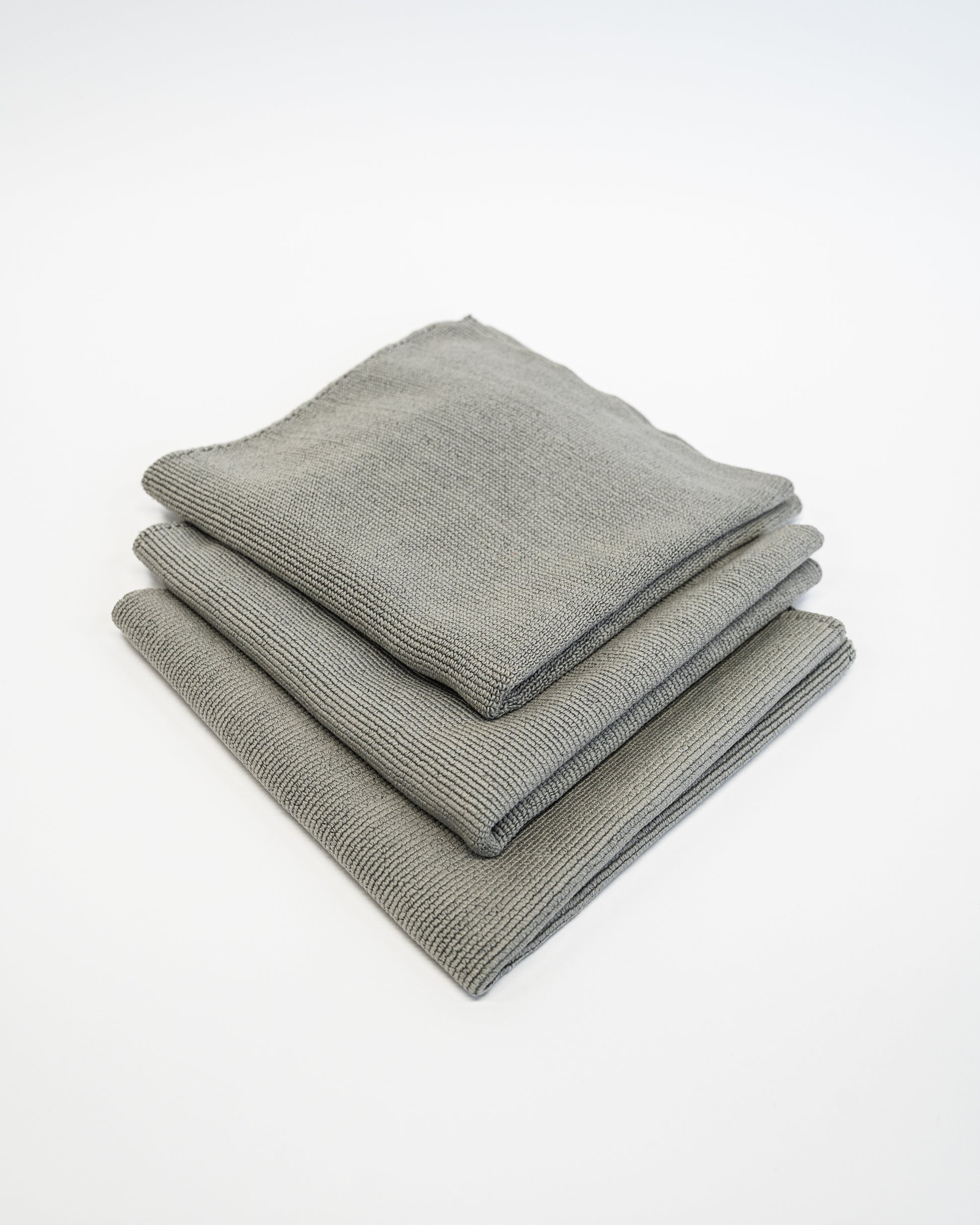 Three neatly stacked FibreKing Soft Edgeless Multi-Purpose Microfibre Cloths in gray lie on a white surface, ideal for streak-free detailing on any surface.