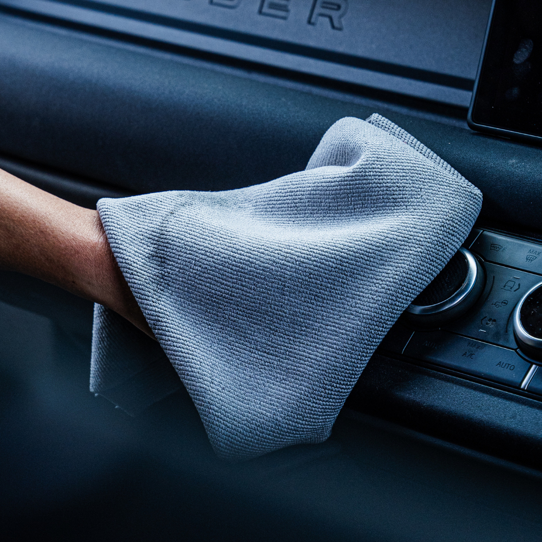 A hand uses the FibreKing Soft Edgeless Multi-Purpose Microfibre Cloth in grey to detail a vehicles dashboard controls.
