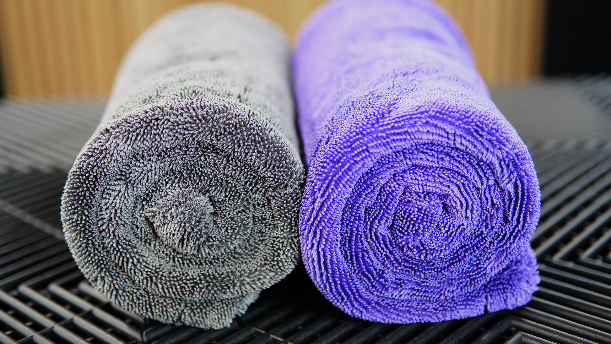 Two rolled FibreKing Silver Label Drying Towels, one gray and one purple, are placed side by side on a black textured surface.