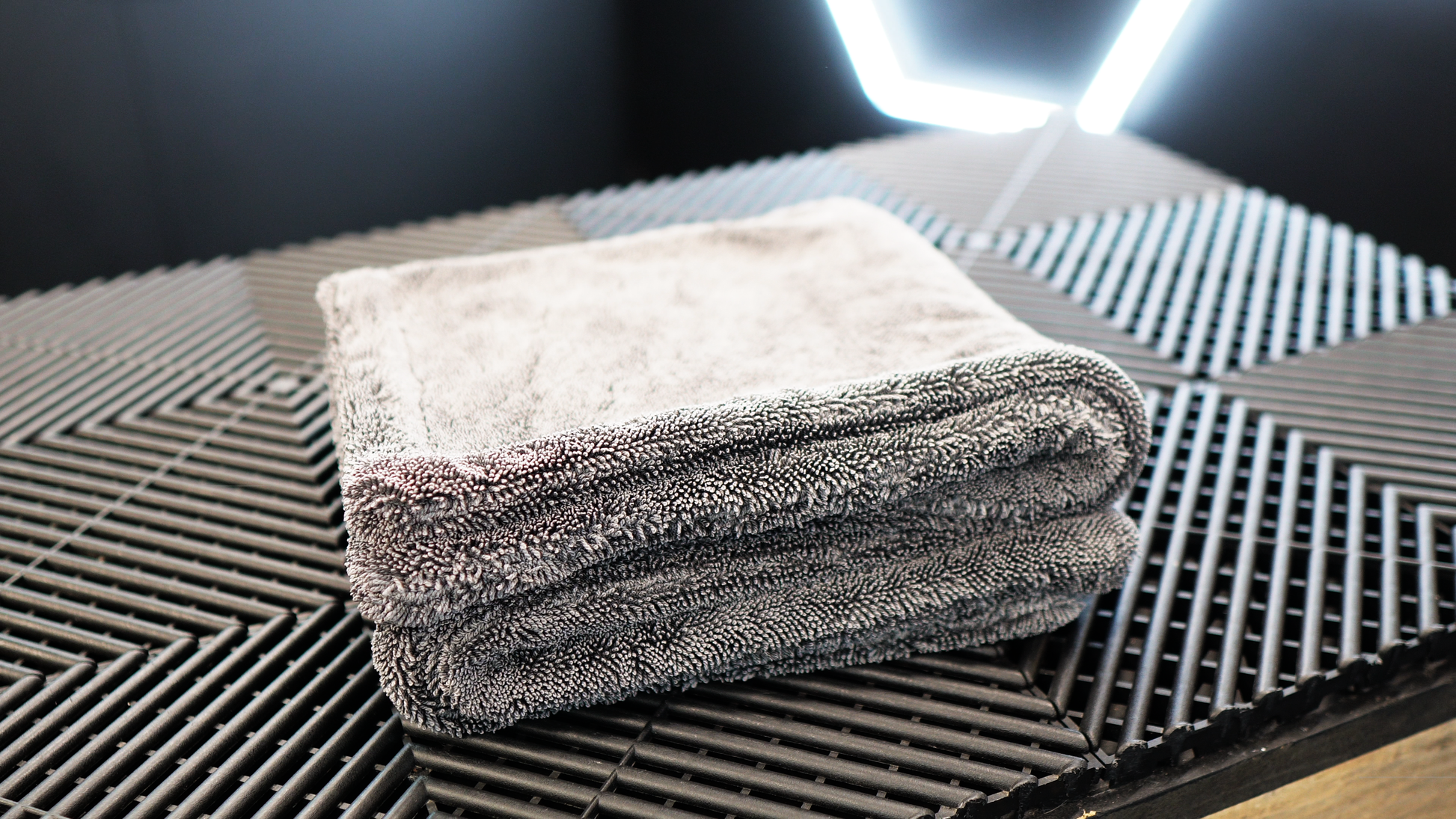 A neatly folded FibreKing Silver Label Drying Towel sits on a black textured surface, illuminated by a geometric light in the background.