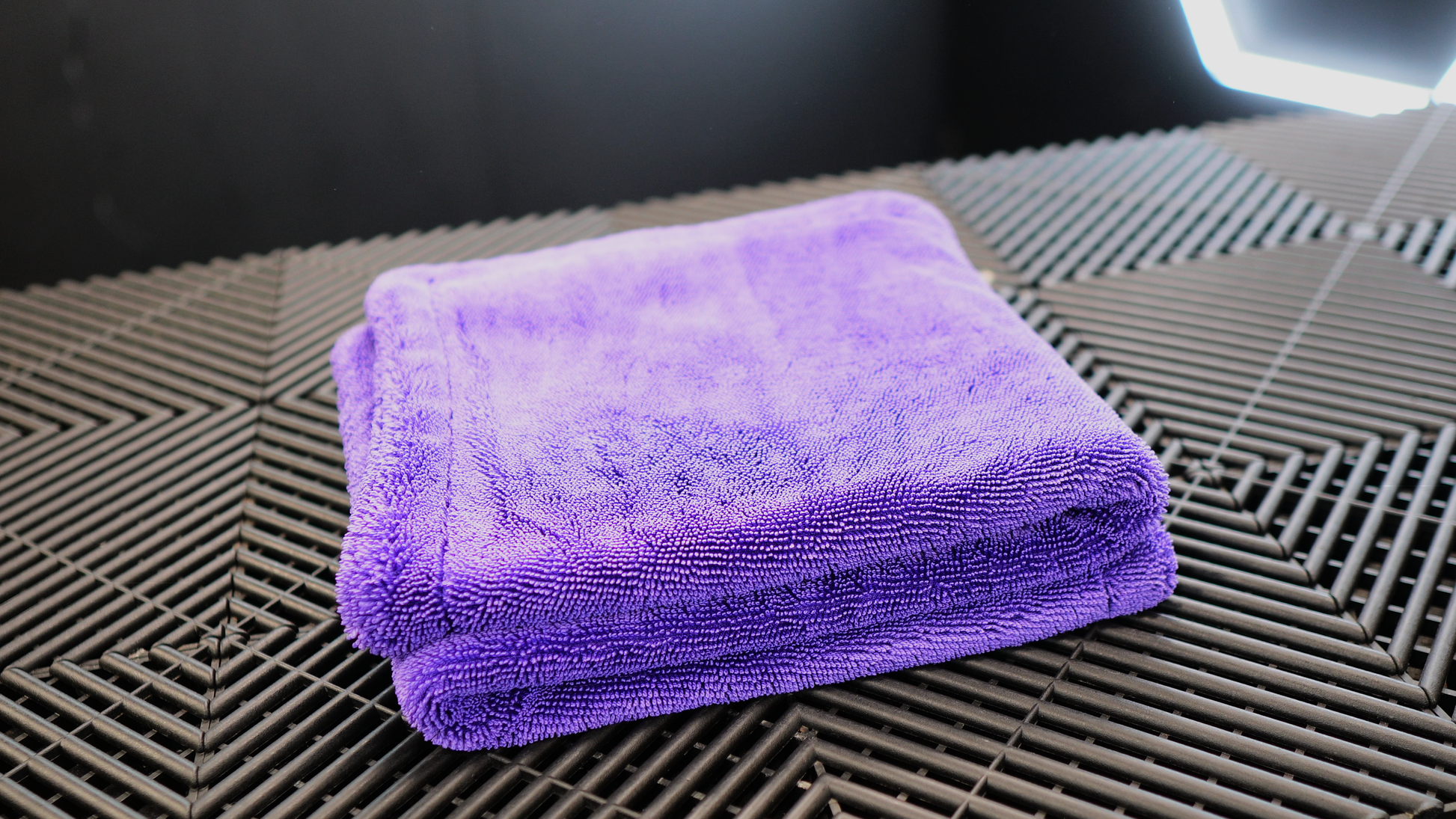 A neatly folded FibreKing Silver Label Drying Towel in purple rests on a black textured surface with geometric patterns.