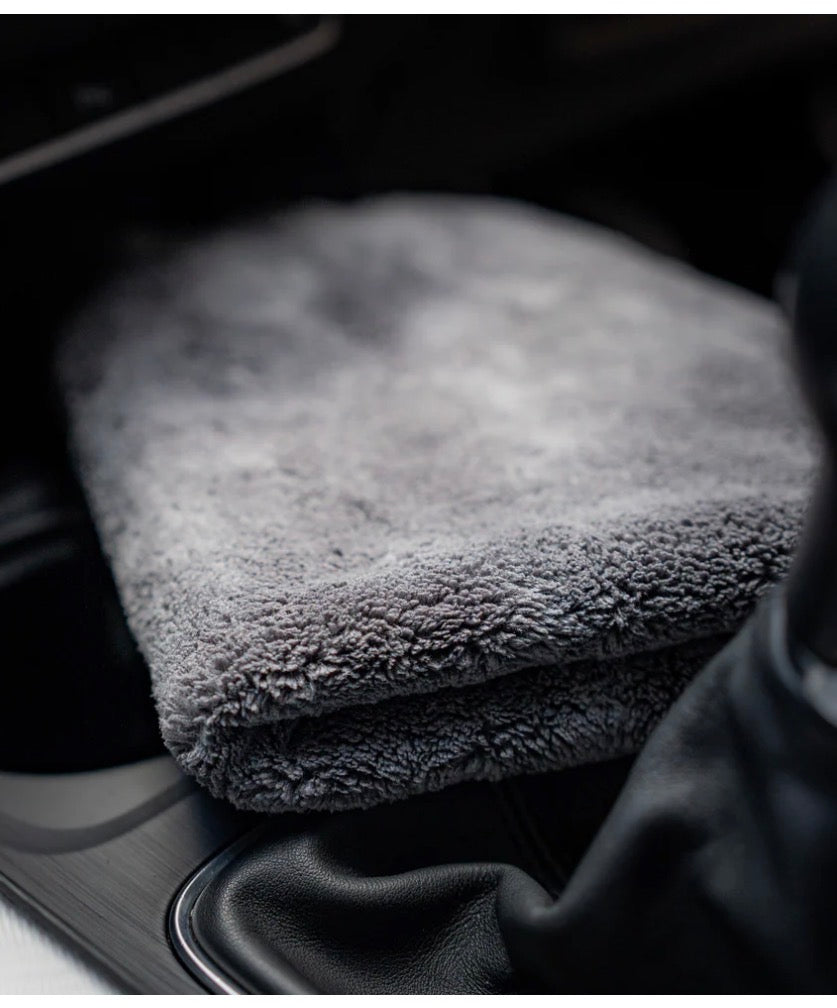 A folded FibreKing Ultimate Detailer Cloth in soft grey rests on a car’s center console near the gear shift and cup holders.