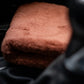 A folded FibreKing Ultimate Detailer Cloth in brown, from the 3 pack set, rests on a dark surface—possibly inside a vehicle—with part of a gear shift visible in the foreground.
