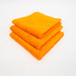Three orange FibreKing Duplex edgeless cloths (3 pack) are neatly folded and stacked on a white surface.