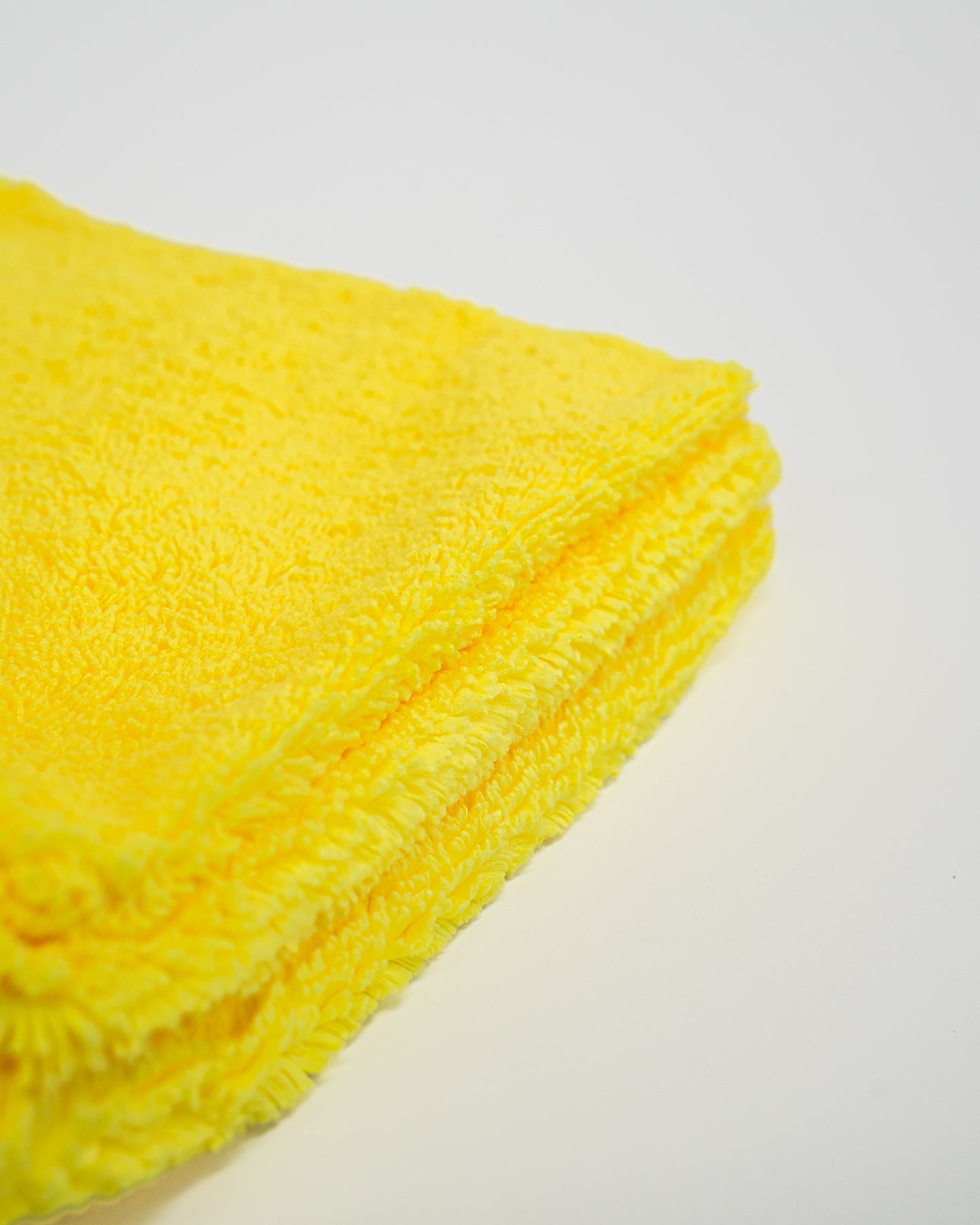A close-up of a folded yellow Duplex Edgeless Cloth from FibreKing, shown on a white surface—this dual pile microfiber towel comes in a 3 pack and is perfect as a detailing cloth for spotless cleaning.