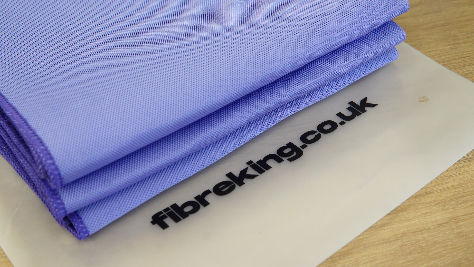 A folded Gold Label Korean Glass Cloth from FibreKing lies on a translucent mat with fibreking.co.uk printed in black, offering streak-free cleaning and high absorption. Pack contains 3 premium microfibre cloths.