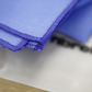 A close-up of FibreKing Gold Label Korean Glass Cloths (3 Pack) stacked on a printed sheet, showcasing their blue microfibre material known for high absorption and streak-free cleaning.