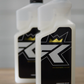 Two white FibreKing Microfibre Wash bottles with black labels and crown graphics sit on a wooden surface. This premium solution keeps your microfibre towels fresh and effective for detailing.