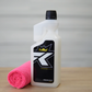 A bottle of FibreKing Microfibre Wash with a black label and gold crown logo stands next to a rolled pink microfibre cloth on a wooden surface, ideal for caring for your microfibre towels.