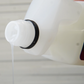 A close-up of FibreKing Microfibre Wash, a white plastic bottle pouring clear liquid, perfect for microfibre towel care, with a blurred light background.