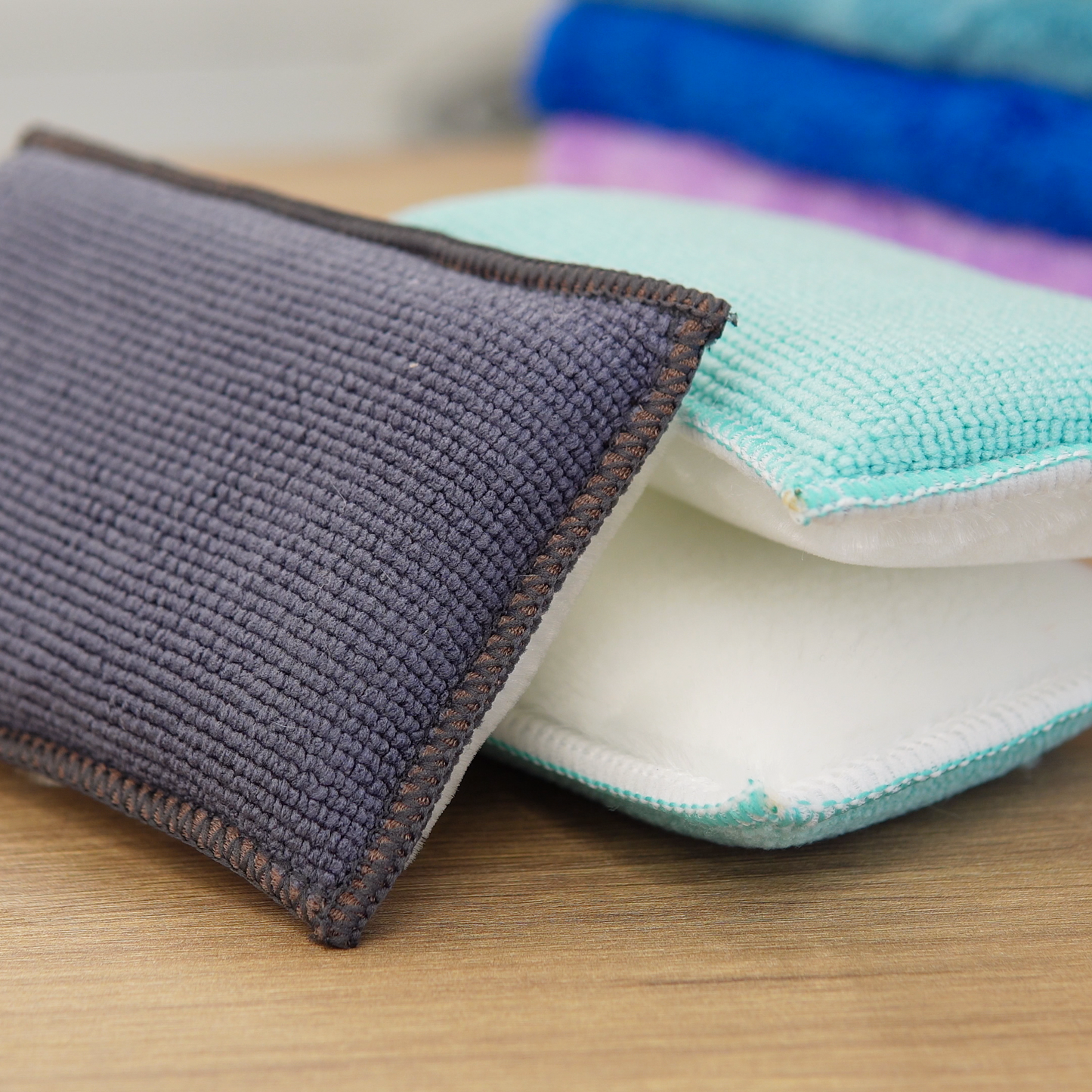 Close-up of two rectangular FibreKing Scrub Pads 2 pack, perfect for any car cleaning kit, resting on wood. Additional blue and purple pads are seen blurred in the background.