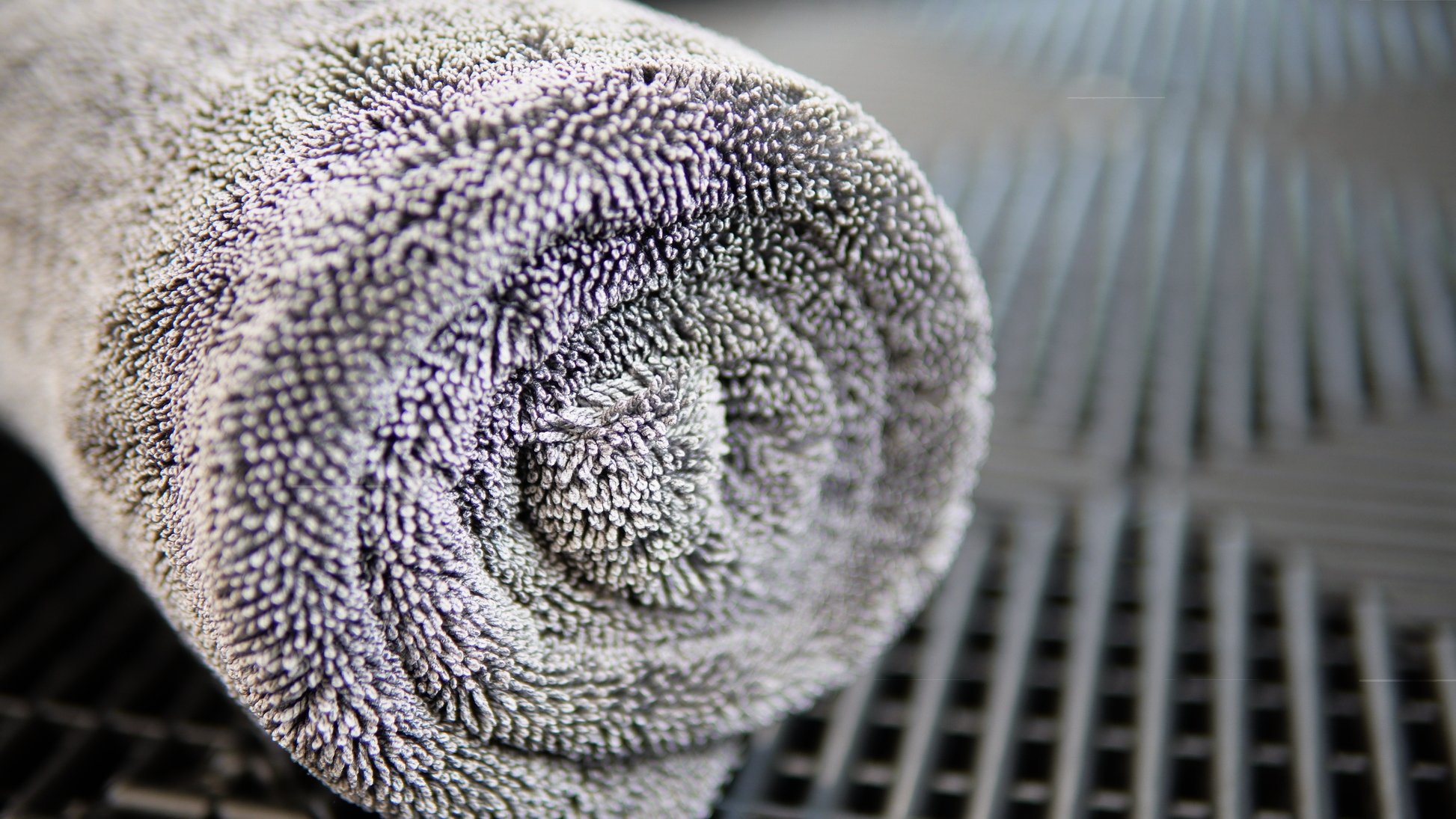 A close-up of a rolled Silver Label Drying Towel by FibreKing on a dark, textured surface emphasizes its premium quality for car detailing.