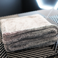 A neatly folded FibreKing Silver Label Drying Towel sits on a black textured surface, illuminated by a geometric light in the background.