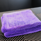 A neatly folded FibreKing Silver Label Drying Towel in purple rests on a black textured surface with geometric patterns.